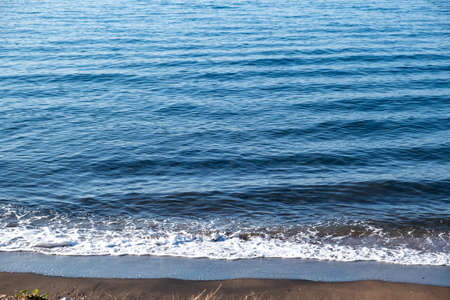 Summer holiday concept. Blue calm sea background meets the sandy beach. Foam and reflections on the...