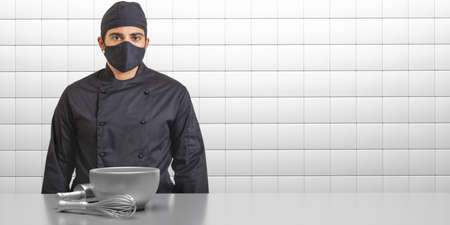 Chef in coronavirus days. Man in cook uniform with black face mask, kitchen interior background. COVID19 safety in restaurant food preparationの写真素材