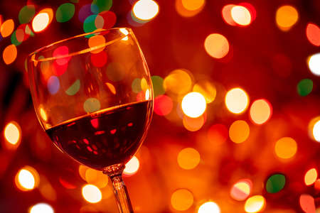 Red wine glass against christmas lights colorful bokeh background, closeup view. Holiday greeting card template, copy spaceの写真素材