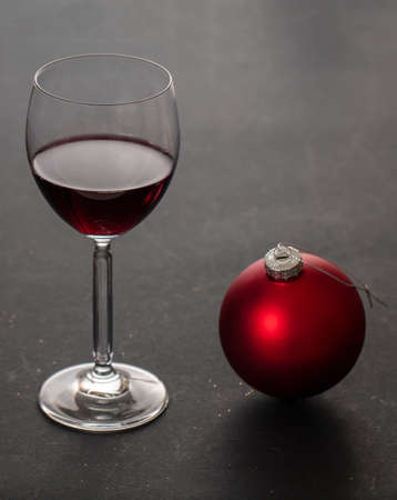 Christmas red wine. Wineglass and red xmas ornament bauble, black background, closeup vertical view....