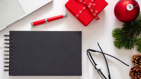 Christmas, office closed. Business desk flat lay, holiday card template. Blank black notebook, laptop and red color xmas decoration on white background, top viewの写真素材