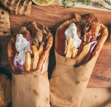 Gyros wraps greek food. Grilled meat sliced with fried potatoes, tomato and yogurt tzatziki in a pita bread, wooden table background, closeup view. Turkish shawarmaの写真素材