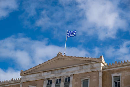 Greek flag waving on pole against cloudy blue sky background, copy space. Greece national sign symbol on Parliament building topの写真素材