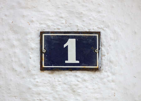 Street number one. Digit 1 on metal vintage plate mounted on whitewashed wall. Traditional house...