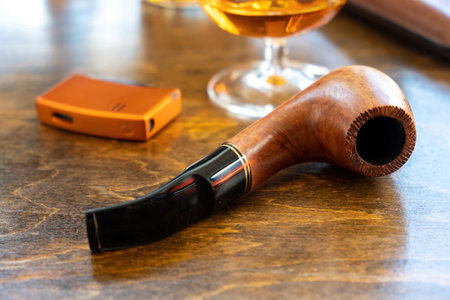 Tobacco pipe on a wooden table, closeup view. Handmade pipe from wood brandy glass and lighter,...
