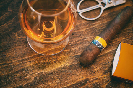 Tobacco and alcohol. Cigar and brandy on a wooden table, closeup view. Cuban quality cigar and whiskey, smoking and drinking luxury lifestyleの写真素材