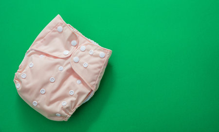 Reusable baby diaper. Eco friendly cloth nappy pink color on green background, top view, copy space. Sustainable lifestyle, zero waste concept.の写真素材