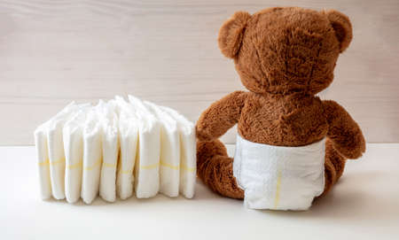 Baby teddy wearing diaper sitting on white color floor, wooden wall background, rare viewの写真素材