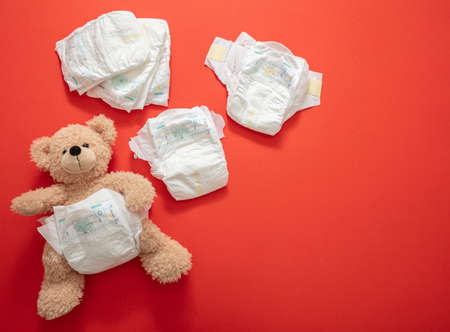 Baby diapers and cute teddy bear on orange color background. Newborn nappies open and closed, top view, copy spaceの写真素材