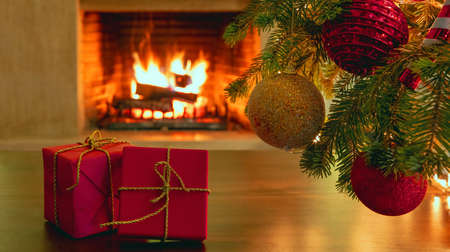 Christmas present, interior room celebration concept. Xmas tree branch with colorful balls, two red gift boxes with golden ribbons, burning fireplace background. Warm family moments.の写真素材