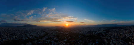 Sunset over Athens, Greece. Aerial drone panoramic view from Penteli mount. Last sunbeams over Greek capital background. Destination Athens, where sunrays caress, heat up people and hearts, banner.の写真素材