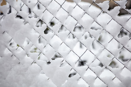 Wire mesh covered with snow, winter seasonal abstract background texture. Metal fence in white...