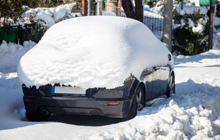 Car covered with snow background. Automobile parked, stuck at urban street a winter day. Snowfall problems concept. Sun shines and tries to melt the snow from the frozen trapped vehicle.の写真素材