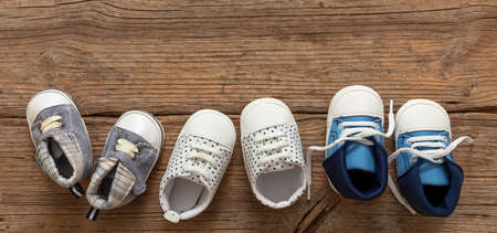 Baby first steps. Three pairs of boy shoes variety on wood floor background, top view. Kids...