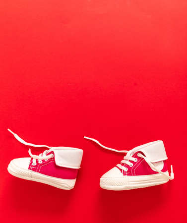 Kids first steps. Baby sport shoes walking on red color background. Child small size sneakers, canvas booties. Space, card invitation templateの写真素材