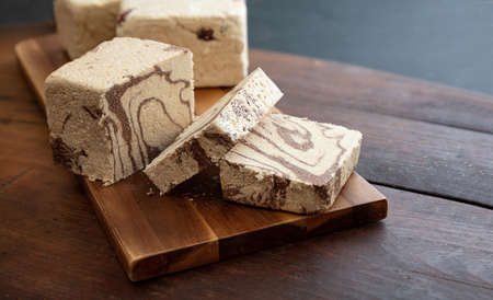 Halva cocoa and sunflower seeds pieces on wooden table background. Chocolate halvah or halwa,...