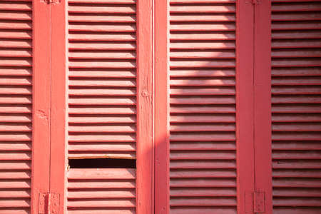 Wooden shutters. Closed, aged, retro red color window shutters for background, texture. Traditional damaged weathered wood structure sunny day,の写真素材