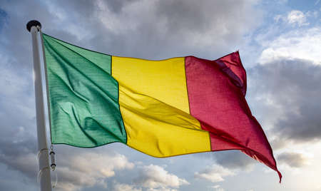 Mali sign symbol. Mali national flag on a pole waving against cloudy sky background.の写真素材
