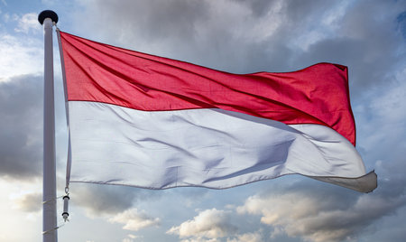 Indonesia sign symbol. Indonesian national flag on a pole waving against cloudy sky background.の写真素材