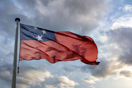 Samoa sign symbol. Samoan national flag on a pole waving against cloudy sky background.の写真素材