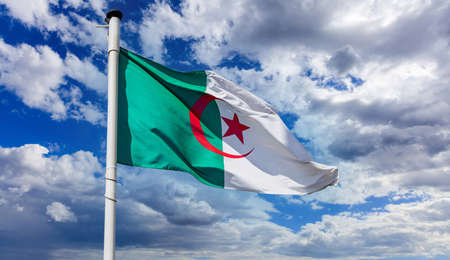 Algeria flag, Algerian national symbol on a flagpole waving against blue cloudy skyの写真素材
