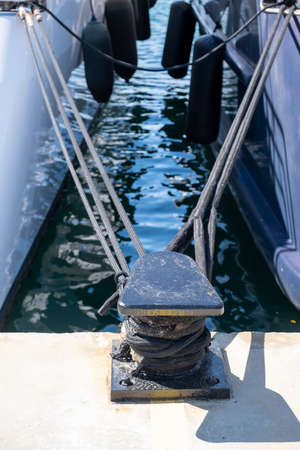 Mooring ropes tied on black metal steel bollard. Secured moored yachts at harbor quay at marina...