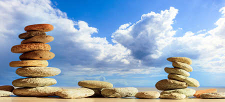 Zen stones stacked on blue cloudy sky, sea water, beach for background. Pebble pyramid, yoga, meditation and equilibrium, harmony, balance, alternative therapy, Buddhism philosophy. Copy space.の写真素材