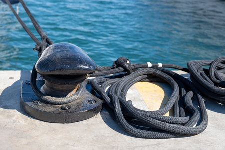 Mooring rope and bollard on sea water and yachts background. Boat heavy duty ropes on black mooring...