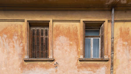 Worn open and closed shutters windows on abandoned residential building facade. Two windows on dirty...