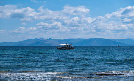 Traditional fishing boat sailing in rippled sea background. Blue and white trawler in the middle of Aegean sea a cloudy day. Fishery at nature, job, sport, hobby, summer holidays in Greece.の写真素材