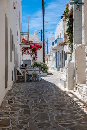 Greece, Kimolos island. Cyclades. May 18, 2021. Two men at a cafe, Chora village. Greek traditional architecture whitewashed buildings and narrow cobblestone street. Sunny day, clear blue skyのeditorial素材