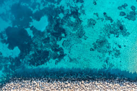 Breakwater and turquoise blue color sea background, aerial drone top down view. Rocky protection wall on clear rippled water, Cyclades Koufonisi island harbor. Greeceの写真素材