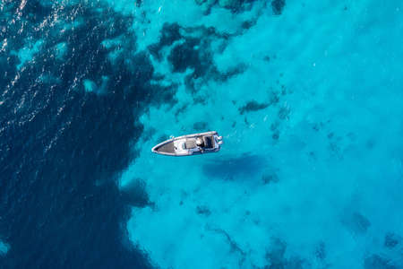 Inflatable boat on turquoise blue color sea background. Aerial drone top down view. Motorboat  cruising slowly on rippled water. Cruising Aegean Sea, Greek islands summer vacations, destination Greeceの写真素材