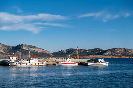 Greece. Koufonisi island, Cyclades, May 22, 2021. Moored white fishing boats at dock. Lighthouse on...