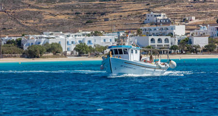 Koufonisi island, Cyclades, Greece. May 23, 2021. Sailing fishing boat in blue Aegean sea. Sandy beach sunny day mountains traditional village background. Summer destination for vacation.のeditorial素材