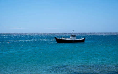 Boat white and blue color moored in the open sea. Wooden vintage vessel, clear blue sky and calm...