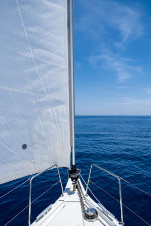 White sloop rigged yacht sailing in open calm ocean, blue sky background, sunny day. Sailboat deck,...