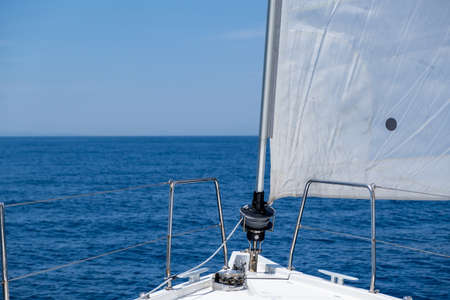 White sloop rigged yacht sailing in open calm ocean, blue sky background, sunny day. Sailboat deck,...