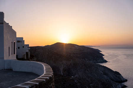 Folegandros island at sunset. Cyclades, Greece. Breathtaking view over the Aegean sea from high cliffs at chora village, Sun shine on orange color sky, calm rippled sea waterの写真素材