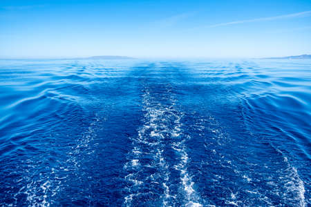 Boat wake, prop wash foam, blue calm sea and clear sky background, view from the ship. Sailing in Aegean seaの写真素材