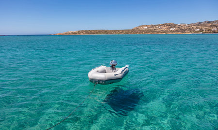 Inflatable dinghy boat on turquoise sea water, island coast and blue sky background, Empty small service tender vessel with motor. Summer cruise in Cyclades Aegean sea Greece,の写真素材