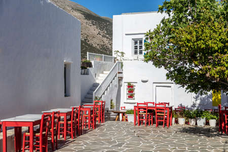 Vacation break time at Sifnos island, Greece. Traditional tavern cafe restaurant chairs and tables on cobblestone empty sunny yard. Whitewashed walls of building plants background. Summer destination.の写真素材