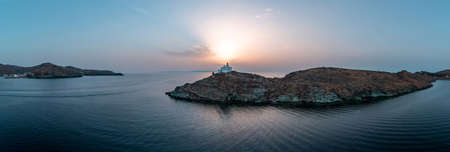 Kea Tzia island. Greece, Cyclades. Lighthouse on a rocky cape at sunset, Drone, aerial view panorama.  Korissia port and rippled sea water background. Summer holidays destination.の写真素材