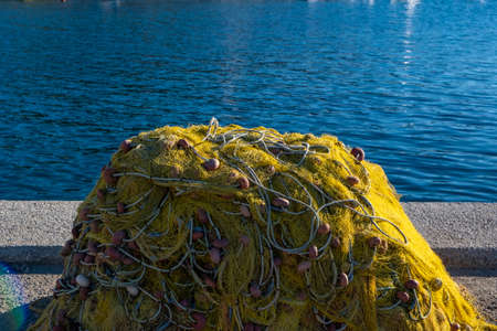 Fishing nets stack on the fisher port dock drying under the sun. Yellow color fishnets with ropes...
