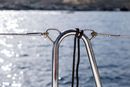 Boat railing detail. Black rope tied on stainless steel guard rail, blur shiny sea water surface....