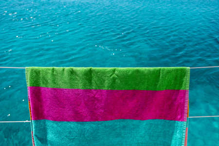 Beach towel drying on clothesline, blur sea background. Colorful towel hanging on boat stainless...