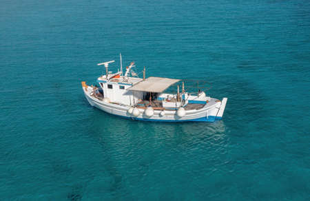 Fishing boat on turquoise blue color sea background. Aerial drone view. Blue and white traditional...