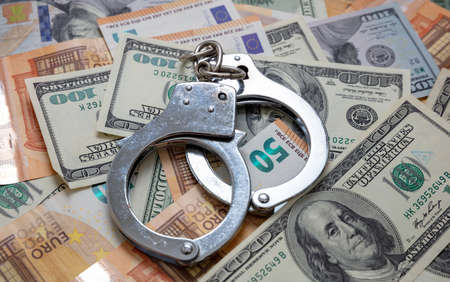 Money and crime. Handcuffs on US dollars and euro banknotes background. Bribe, corruption and...