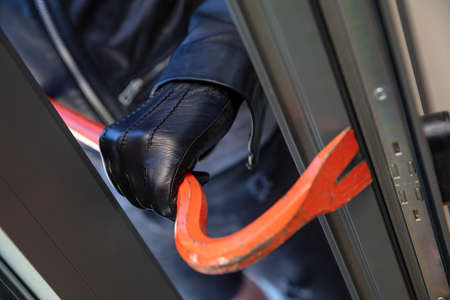 Housebreak with crowbar. Burglar wearing leather gloves breaking a glass aluminum door. Masked thief...