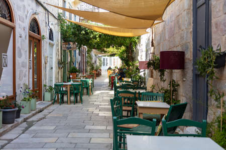 Syros island, Cyclades, Greece. May 27, 2021. Traditional outdoor cafe tables and chairs at cobblestone street, Ermoupolis capital town. Summer leisure destination.のeditorial素材